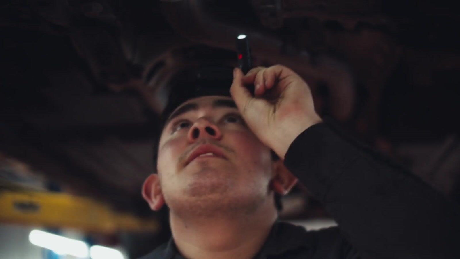 A technician under a raised vehicle, wearing the Marv camera headset, inspecting the underbody by torchlight
